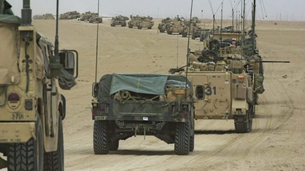 A convoy of US military armored personnel carriers and Humvees advancing through the Iraqi desert, illustrating how strategic fears of a Power Vacuum keep the US military tied to the Middle East.