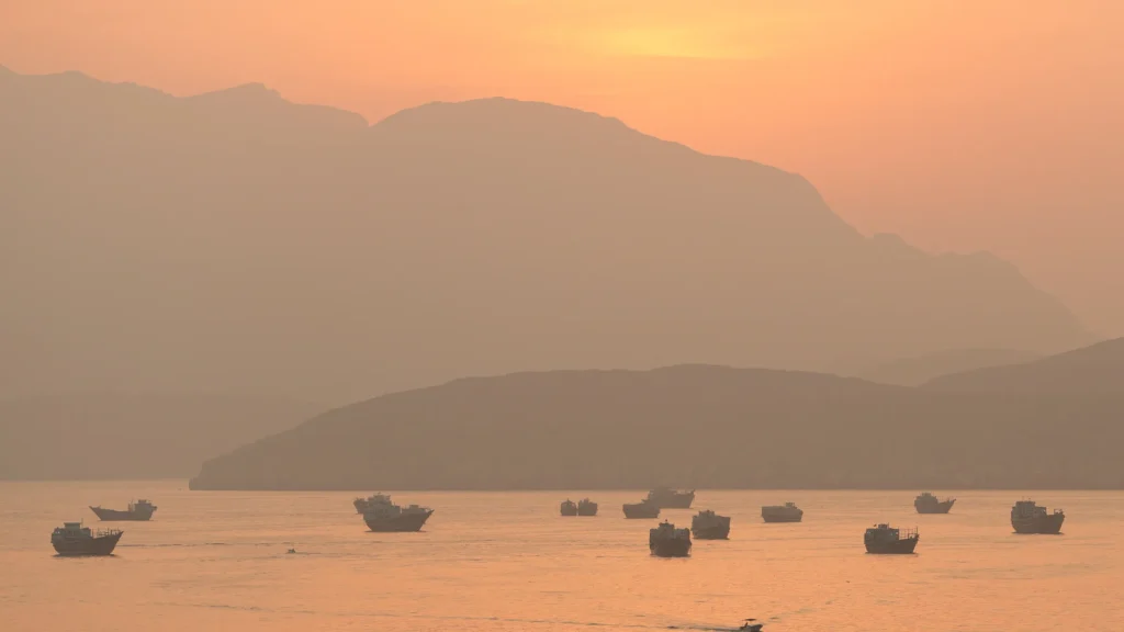 سلاح هرمز الاقتصادي: الميزة الحاسمة لإيران على أمريكا Small maritime vessels anchored at sunset in the Strait of Hormuz near Musandam, illustrating how Tehran leverages the Hormuz Economic Weapon against global energy markets.