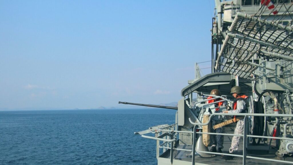 US Navy sailors standing watch at a naval autocannon on a warship deck in the Persian Gulf, illustrating how Middle East conflict impacts East Asia Deterrence.