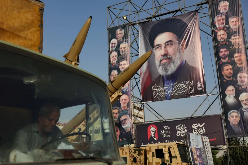 استراتژی جنگ ایران: چرا تحریمها نمیتوانند تسلیم را بهدنبال داشته باشند Ballistic missiles displayed on military launcher trucks in Tehran below a large billboard featuring Iran's Supreme Leader Mojtaba Khamenei, illustrating defense posture and resilience under the Iran War Strategy.