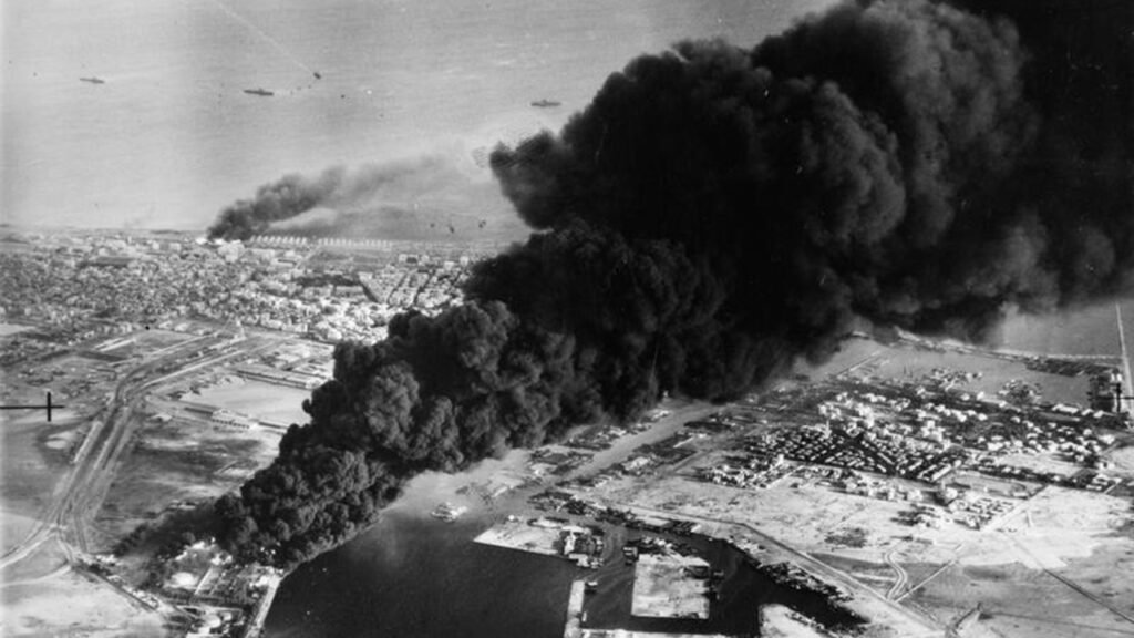 Thick black smoke rising over Port Said and the coastline during the Franco-British invasion, reflecting historical military lessons from the Suez Crisis.