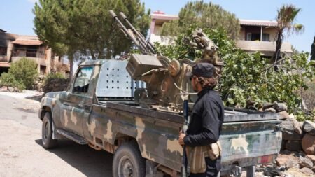 A camouflaged pickup mounted with a twin-barrel anti-aircraft gun sits on a Suwayda street, a man in black holding a rifle beside it — the militarized reality the article says would turn any Druze State into a narco proto-state.