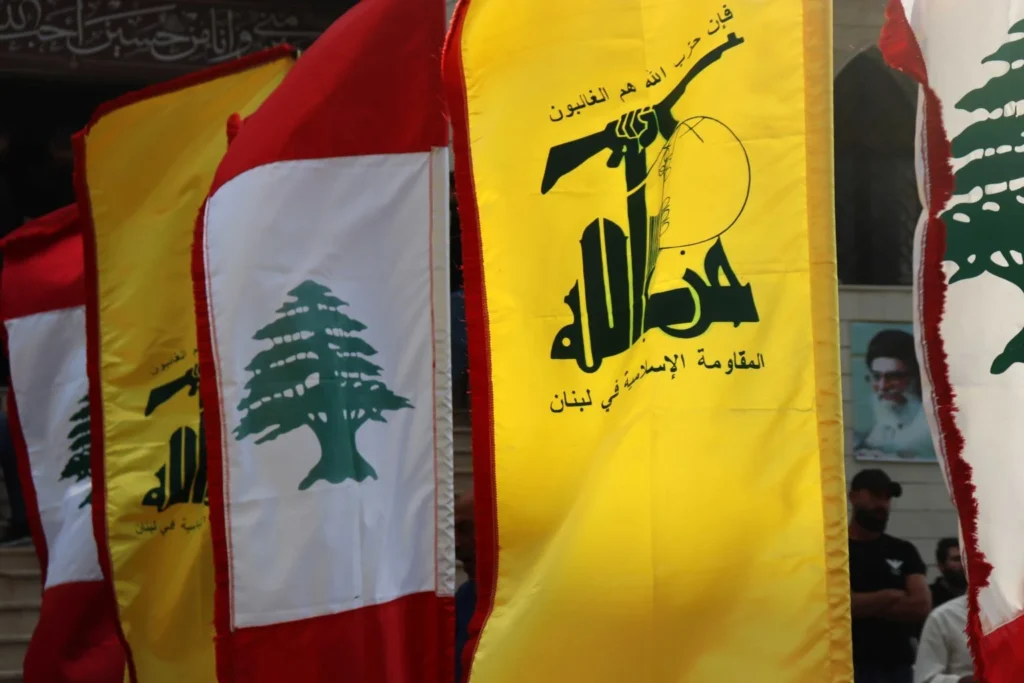 Hezbollah Liaison Chief Abdallah Tests Lebanese Authority Hezbollah and Lebanese flags flying side-by-side with a portrait of Hassan Nasrallah, illustrating how the Hezbollah Liaison Chief tests Lebanese authority.