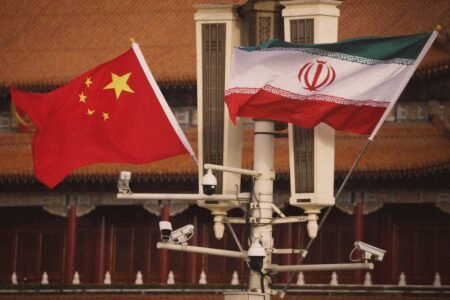 Chinese and Iranian flags flying with surveillance cameras, illustrating Beijing's diplomatic dilemma in the Yemen Crisis between Tehran and Riyadh.