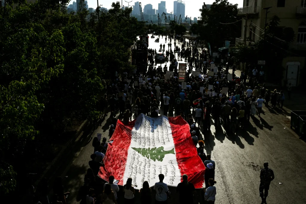 Lebanon Sectarian Rule Endures Through a Wait-and-See Trap Demonstrators carrying a massive Lebanese flag through the streets of Beirut near the port, reflecting public activism against political stagnation under Lebanon Sectarian Rule.