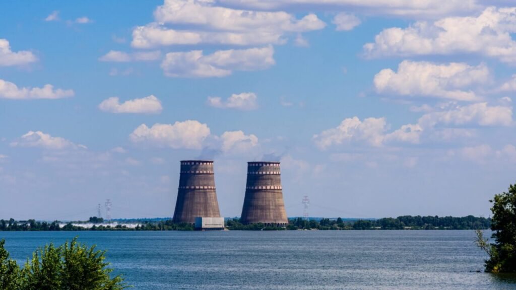 Two massive concrete cooling towers of a nuclear power plant standing near a body of water under a partly cloudy sky, illustrating infrastructure defense considerations for future Saudi nuclear plants.