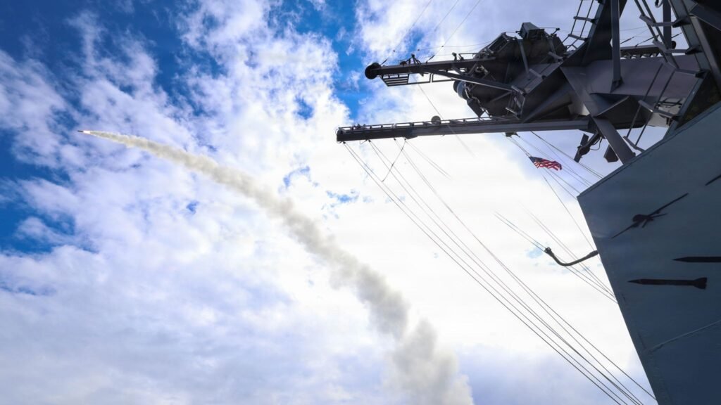 Patriot Interceptors Burned in Iran Leave Asian Allies Exposed A naval air defense missile launching with a smoke trail from a US warship flying the American flag, illustrating stockpile depletion concerns surrounding Patriot Interceptors and Asian security.