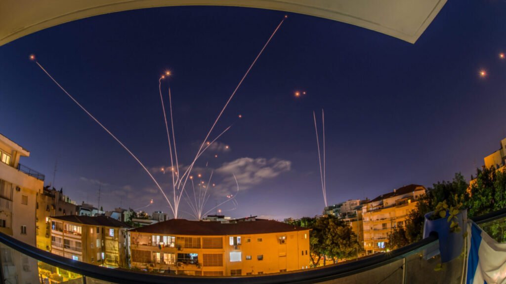 Luminous light trails of air defense interceptor missiles illuminating the night sky over city buildings, illustrating air defense strategies and risks for Iron Dome Imitators targeting modern drone threats.