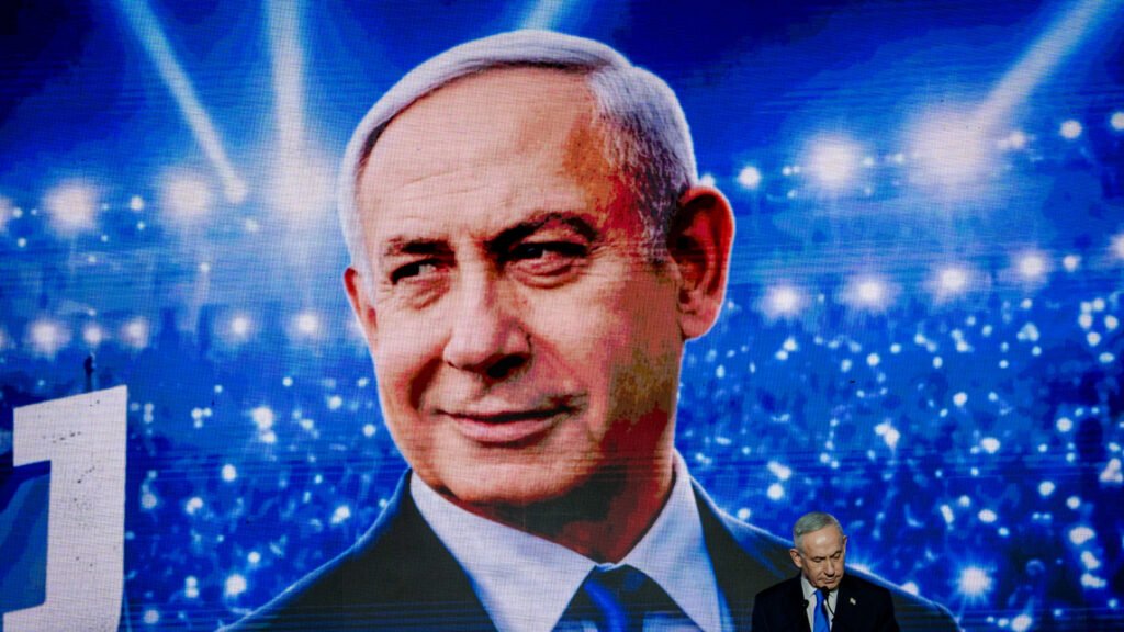 A large screen displaying Benjamin Netanyahu's portrait at a political rally, illustrating the continuity of Israeli Foreign Policy regardless of who wins the vote.