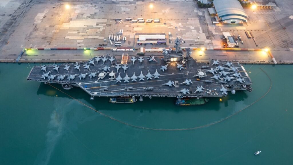 Aerial view of a US Navy aircraft carrier docked at port with fighter jets lined up on its flight deck, demonstrating modern naval power and strategic War Lessons.