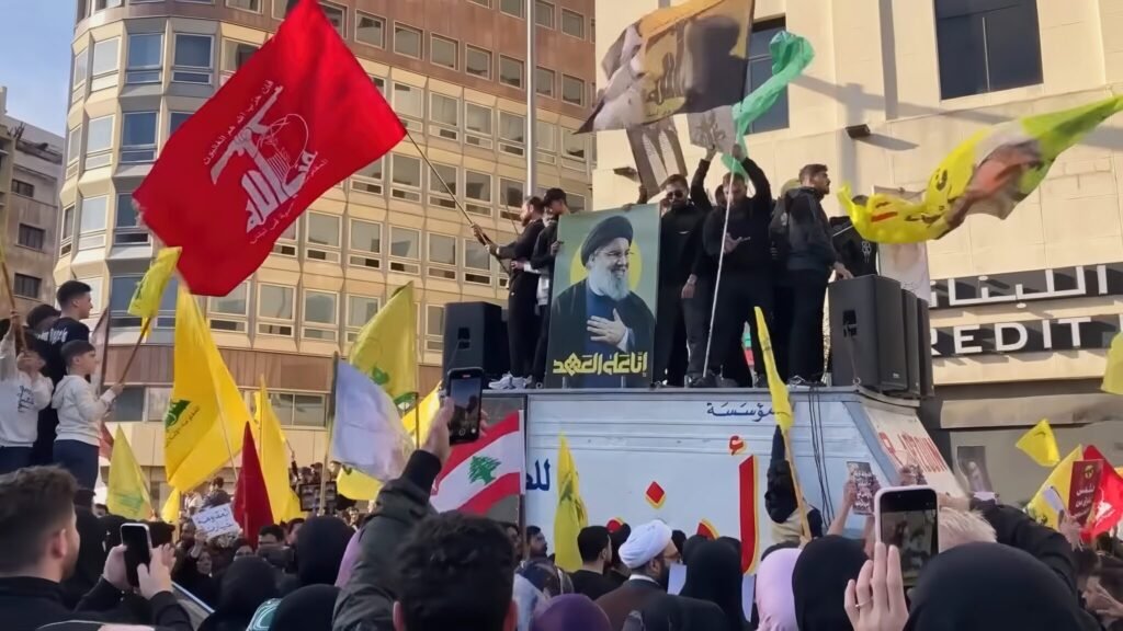 تجدید حیات حزبالله: چرا ضعف قاسم مؤثر است Hezbollah supporters waving flags and displaying a portrait of Hassan Nasrallah during a rally in Beirut, symbolizing the organizational dynamics of Hezbollah Regeneration under Naim Qassem.