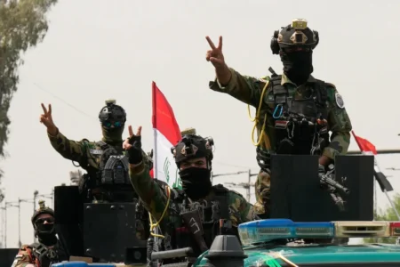 Masked fighters of the Iraqi Resistance Groups in tactical gear raising victory signs atop a vehicle, illustrating why the US exit is perceived as no retreat.