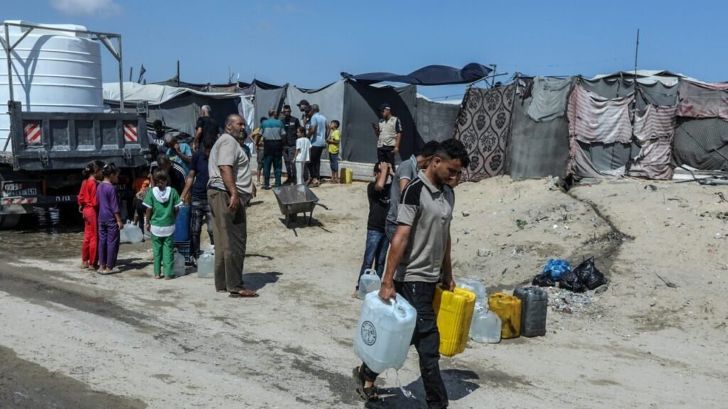 Displaced Palestinians carrying water containers in a makeshift camp in Khan Younis, illustrating the humanitarian toll of the persistent Gaza blockade.