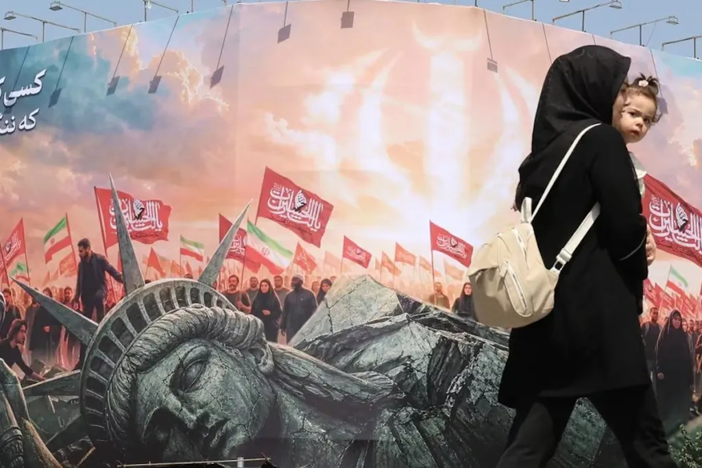 UAE-Iran Back Channel Exposes Critical Cracks in US Backing A woman holding a child walks past an Iranian mural featuring a cracked Statue of Liberty and national flags, illustrating regional diplomacy and the UAE-Iran Back Channel.