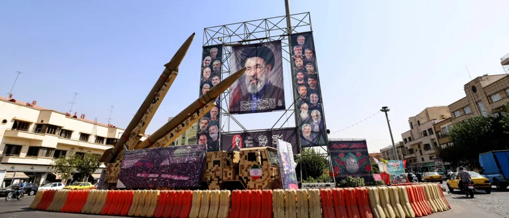 لماذا تستهدف دائرة التصعيد الإيراني الآن البنية التحتية المدنية Large public banners displaying political portraits, including Mojtaba Khamenei, alongside military missile displays in a city square during the ongoing Iran war escalation.