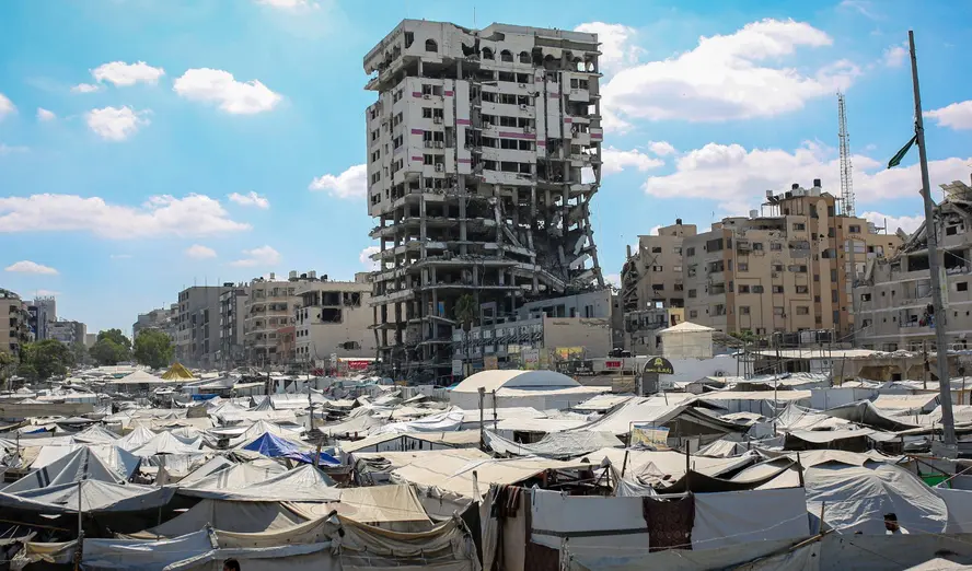Israel Gaza Policy Keeps Hamas in Power, Not Out Displaced Palestinians sheltering in a sprawling makeshift tent camp near a heavily damaged high-rise tower in Gaza City, illustrating the humanitarian crisis and strategic outcomes under Israel Gaza Policy.