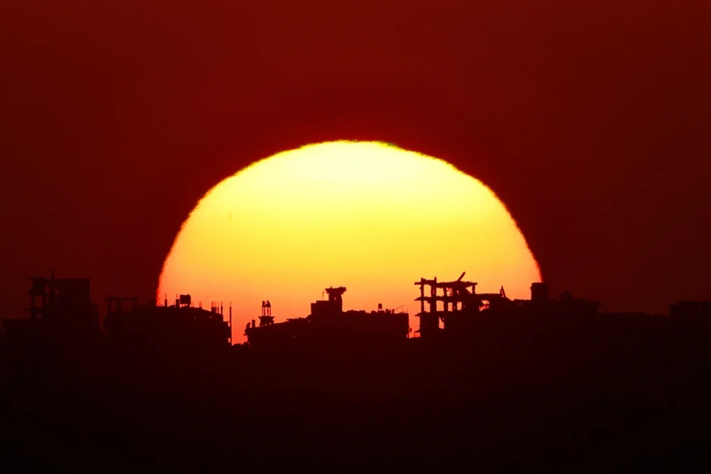 دروس حرب العراق تظهر كيف يمكن لإسرائيل أن تنتصر ومع ذلك تخسر A blood-red sun sets behind the ruined skyline of Gaza, a scene echoing the Iraq War Lessons of winning militarily yet losing strategically.