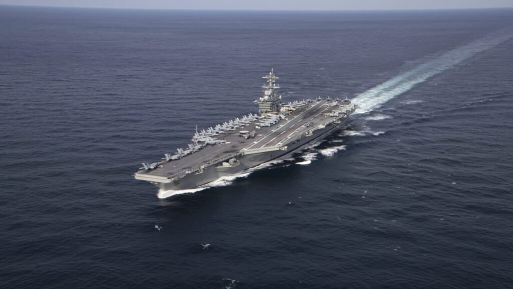 A high aerial view of the aircraft carrier USS Abraham Lincoln underway at sea with naval jets stationed on its flight deck, symbolizing operational strain and the naval Maintenance Crisis.